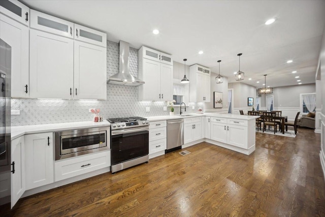 kitchen featuring white cabinets, wall chimney exhaust hood, stainless steel appliances, and decorative light fixtures