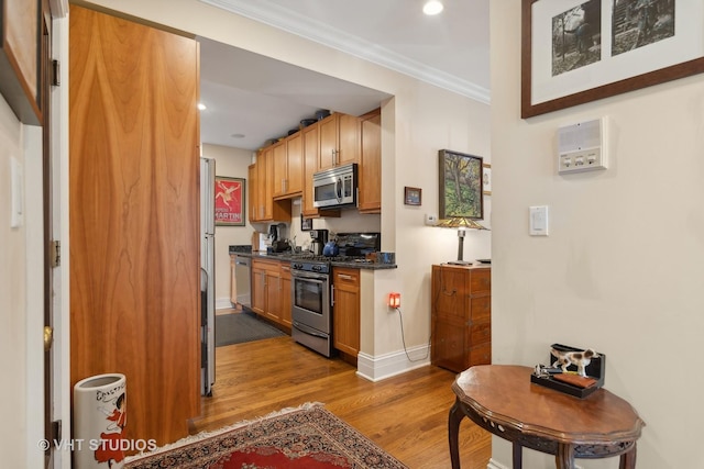 kitchen with appliances with stainless steel finishes, light hardwood / wood-style floors, and ornamental molding