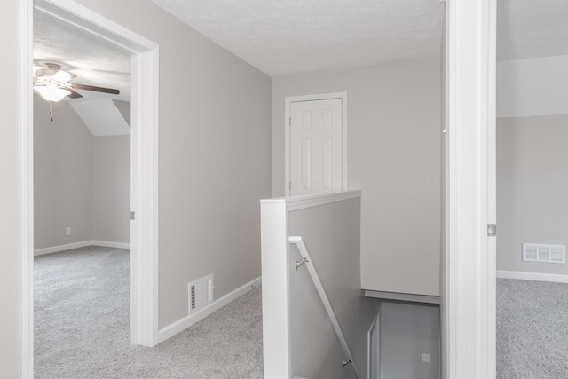 corridor with light colored carpet, vaulted ceiling, and a textured ceiling