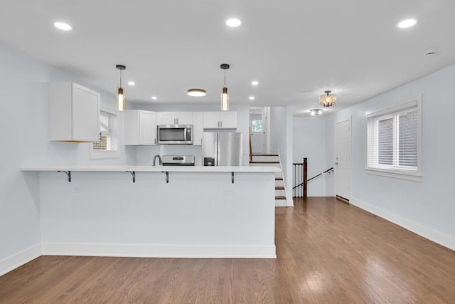 kitchen with white cabinets, a kitchen breakfast bar, hanging light fixtures, wood-type flooring, and stainless steel appliances