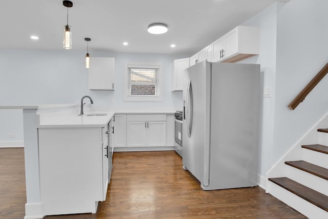 kitchen featuring refrigerator, sink, stainless steel stove, hanging light fixtures, and white cabinetry