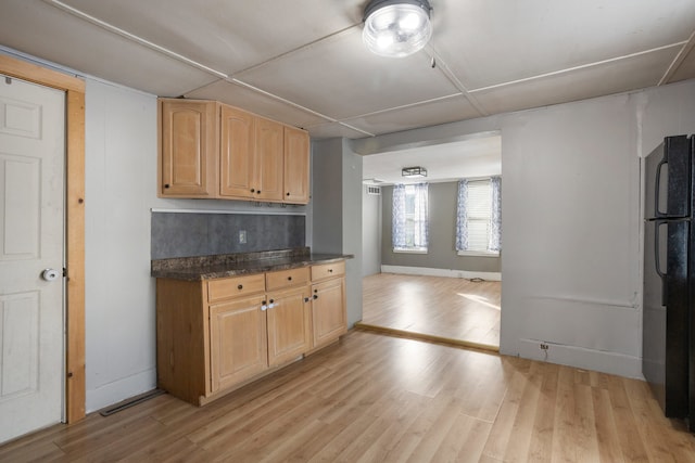 kitchen with decorative backsplash, black refrigerator, light brown cabinets, and light wood-type flooring