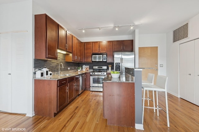 kitchen featuring a breakfast bar, light hardwood / wood-style flooring, dark stone countertops, appliances with stainless steel finishes, and a kitchen island