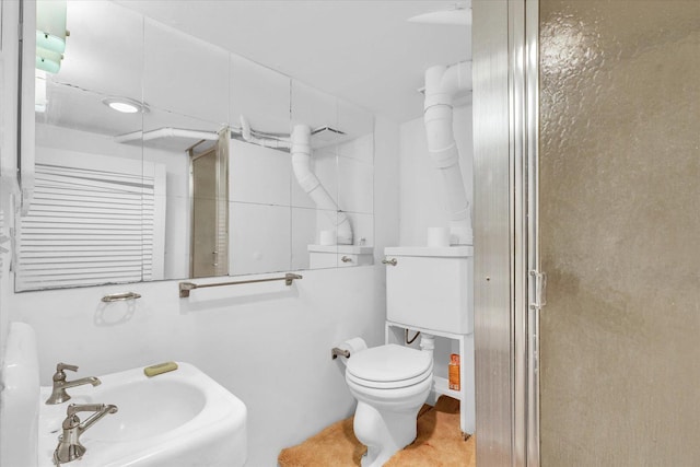 bathroom featuring toilet, a shower with shower door, and sink