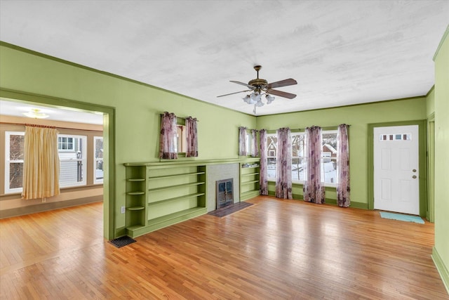 unfurnished living room featuring light wood-type flooring, a brick fireplace, ceiling fan, and a healthy amount of sunlight