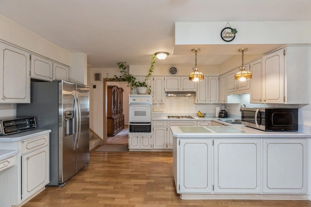 kitchen featuring pendant lighting, backsplash, sink, light wood-type flooring, and appliances with stainless steel finishes