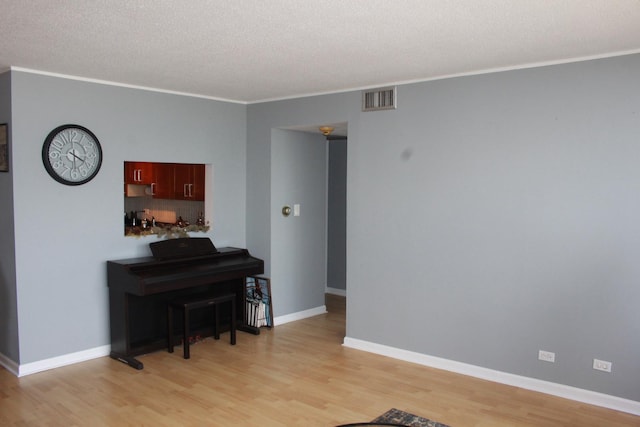 miscellaneous room featuring a textured ceiling, light hardwood / wood-style flooring, and ornamental molding