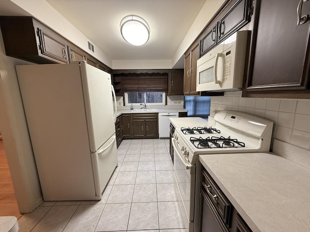 kitchen featuring dark brown cabinetry, sink, light tile patterned floors, and white appliances