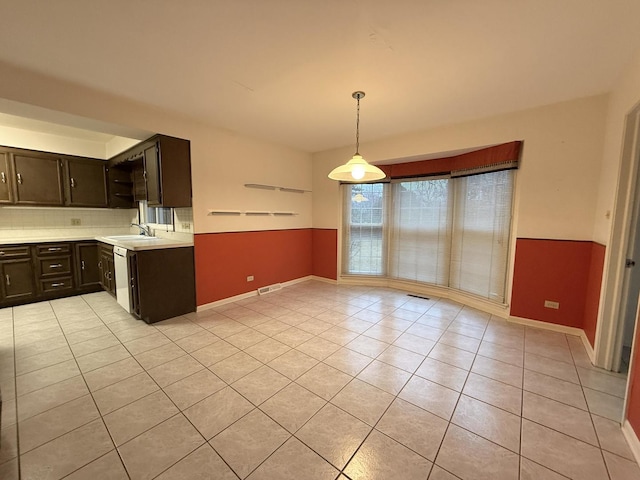 kitchen featuring dark brown cabinetry, sink, light tile patterned floors, dishwasher, and hanging light fixtures