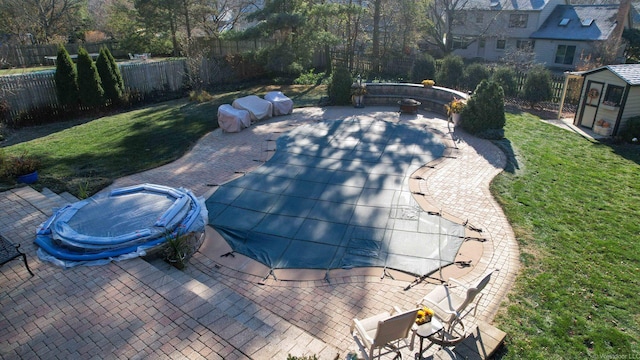 view of pool featuring a hot tub, a storage shed, a patio area, and a lawn