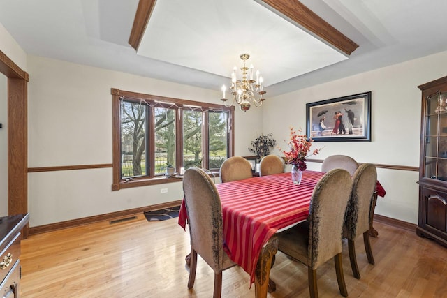 dining room with a notable chandelier, a raised ceiling, and light wood-type flooring