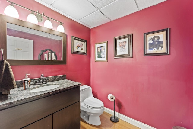 bathroom featuring hardwood / wood-style floors, vanity, a drop ceiling, and toilet