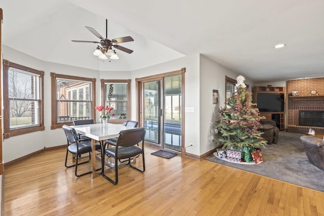 dining room featuring ceiling fan, light hardwood / wood-style floors, a fireplace, and vaulted ceiling