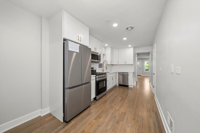 kitchen with white cabinets, backsplash, wood-type flooring, and stainless steel appliances