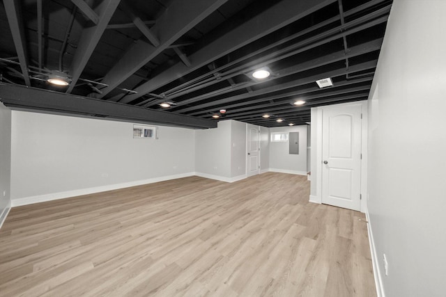 basement featuring electric panel and light hardwood / wood-style flooring