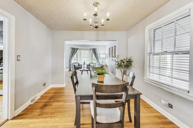 dining room featuring light wood-type flooring, a textured ceiling, and a chandelier