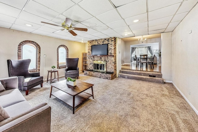 living room with carpet flooring, a paneled ceiling, ceiling fan with notable chandelier, and a brick fireplace