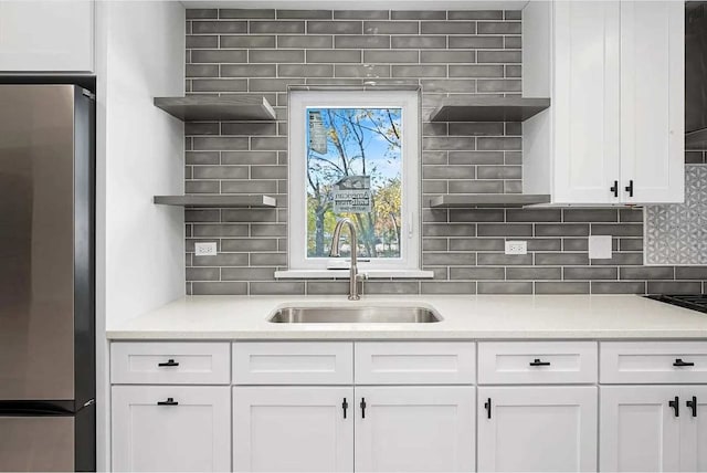 kitchen with white cabinets, stainless steel fridge, decorative backsplash, and sink