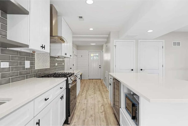 kitchen featuring white cabinets, tasteful backsplash, wall chimney range hood, and stainless steel range with gas stovetop