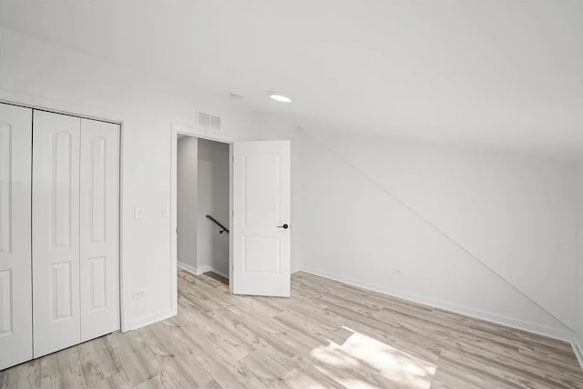 unfurnished bedroom featuring a closet, vaulted ceiling, and light hardwood / wood-style flooring