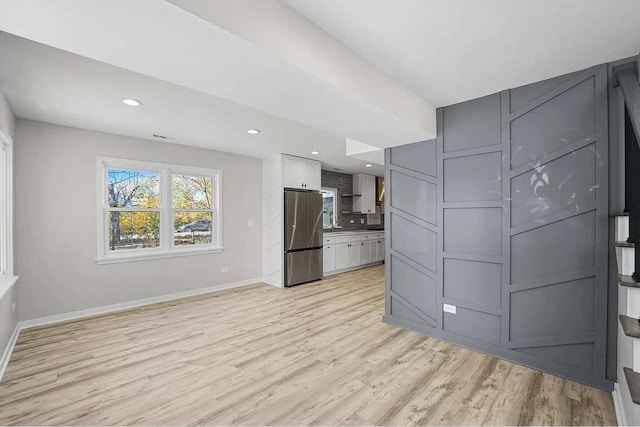 kitchen with backsplash, stainless steel refrigerator, light hardwood / wood-style flooring, and white cabinets