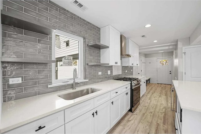 kitchen featuring white cabinetry, sink, wall chimney exhaust hood, light hardwood / wood-style flooring, and stainless steel range with gas stovetop