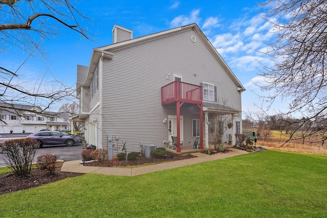 rear view of property with a lawn, a balcony, and central air condition unit