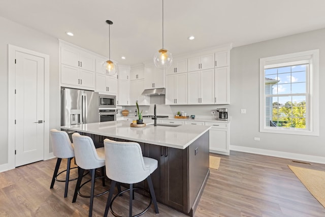 kitchen featuring pendant lighting, white cabinetry, stainless steel appliances, a center island with sink, and light hardwood / wood-style flooring