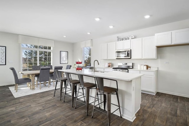 kitchen featuring a healthy amount of sunlight, stainless steel appliances, a center island with sink, and white cabinets