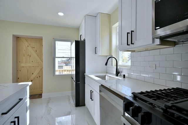 kitchen featuring sink, decorative backsplash, light stone countertops, white cabinetry, and stainless steel appliances