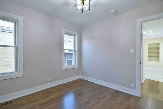 empty room with dark hardwood / wood-style floors and an inviting chandelier