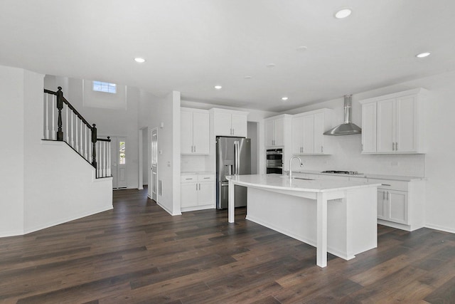 kitchen with white cabinetry, a kitchen island with sink, wall chimney range hood, and appliances with stainless steel finishes