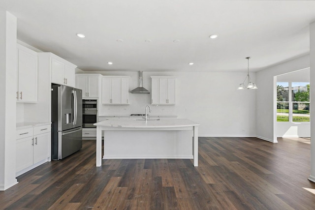 kitchen with white cabinetry, hanging light fixtures, wall chimney range hood, an island with sink, and appliances with stainless steel finishes