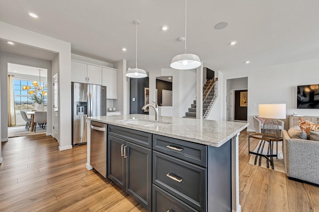 kitchen featuring stainless steel appliances, sink, white cabinetry, hanging light fixtures, and an island with sink