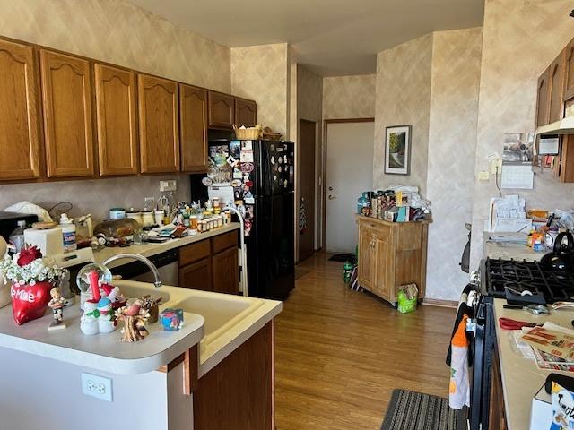 kitchen with black refrigerator, stainless steel gas range oven, kitchen peninsula, and light wood-type flooring