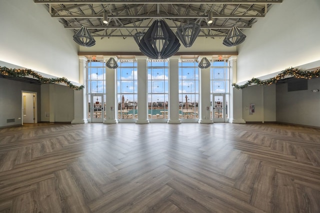 unfurnished living room featuring dark parquet flooring and a towering ceiling