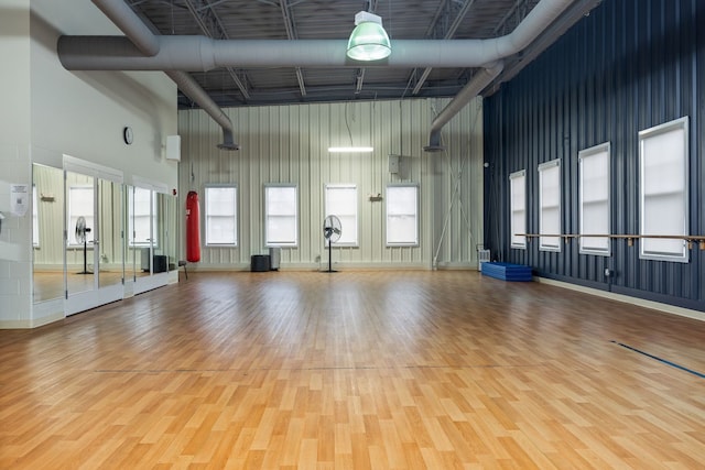 workout room with a healthy amount of sunlight, wood-type flooring, and a towering ceiling