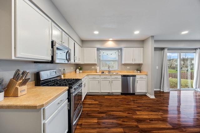 kitchen with appliances with stainless steel finishes, dark hardwood / wood-style floors, white cabinetry, and sink