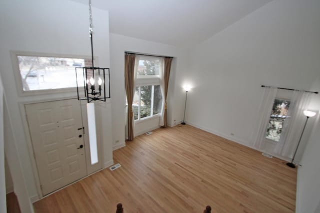 entrance foyer featuring visible vents, baseboards, lofted ceiling, light wood-style floors, and a notable chandelier