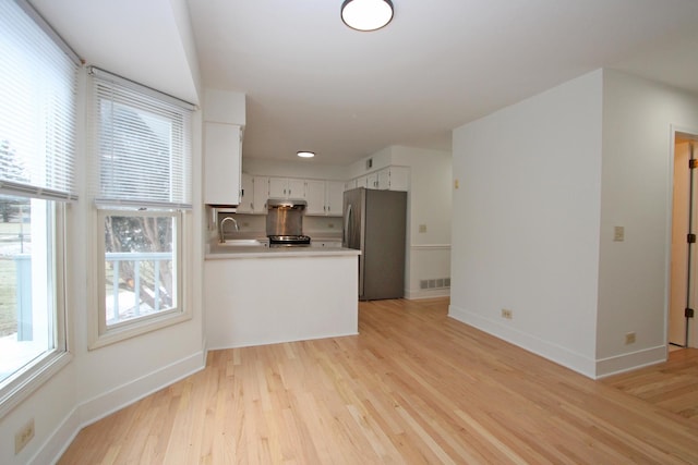 kitchen with kitchen peninsula, stainless steel fridge, light hardwood / wood-style floors, and white cabinetry