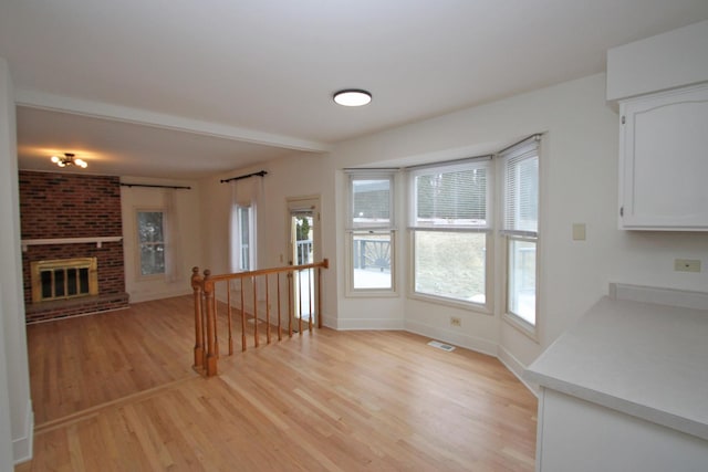 unfurnished living room featuring light hardwood / wood-style flooring and a brick fireplace