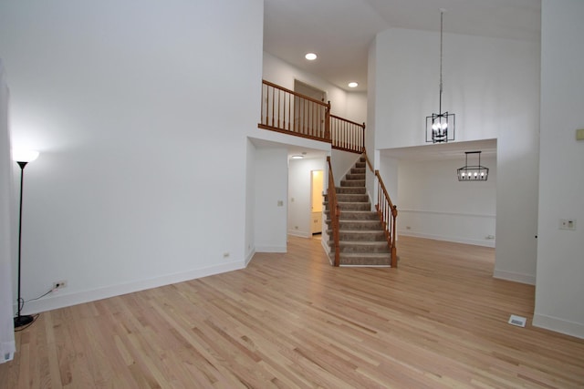 unfurnished living room featuring stairway, wood finished floors, high vaulted ceiling, and a chandelier