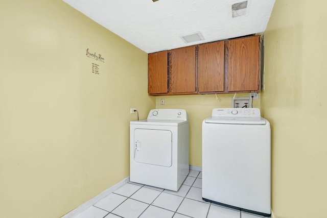 clothes washing area featuring washing machine and clothes dryer, light tile patterned floors, cabinets, and a textured ceiling