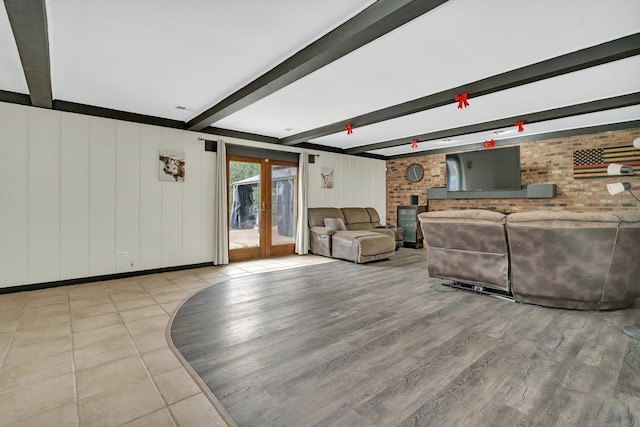 living room featuring beamed ceiling, french doors, light wood-type flooring, and brick wall