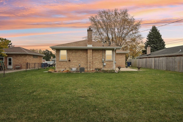 back house at dusk featuring central AC unit and a lawn