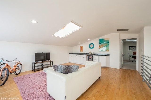 living room featuring wet bar, light hardwood / wood-style flooring, beverage cooler, and lofted ceiling with skylight