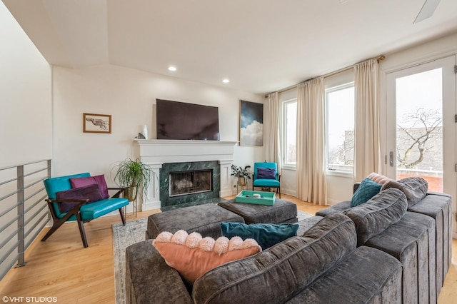 living room with light hardwood / wood-style flooring, vaulted ceiling, and a high end fireplace