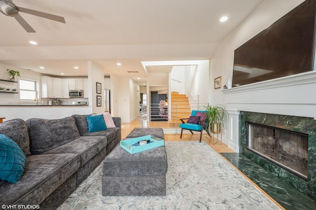 living room with a high end fireplace, sink, ceiling fan, and hardwood / wood-style flooring