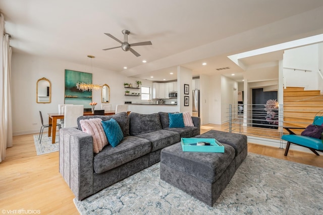 living room with ceiling fan with notable chandelier and light wood-type flooring