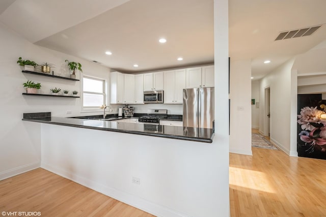 kitchen with kitchen peninsula, stainless steel appliances, light wood-type flooring, white cabinets, and sink